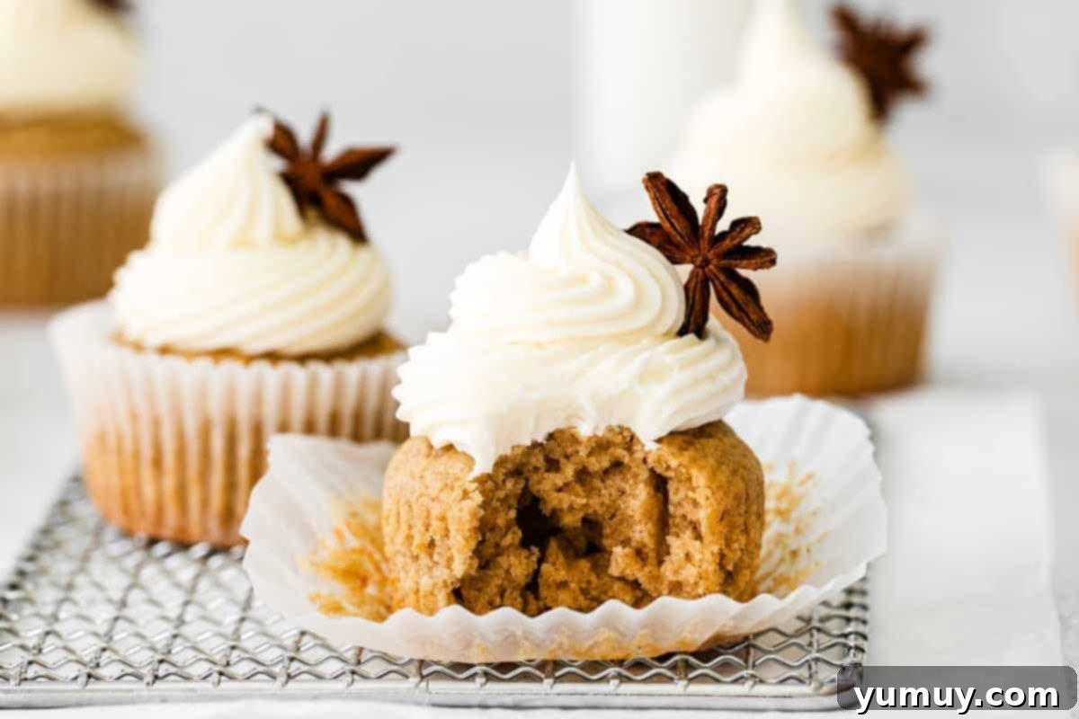 An unwrapped chai cupcake with cream cheese frosting and a bite taken out, resting on a wire rack next to an intact frosted cupcake.