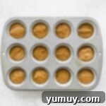 Chai tea cupcake batter carefully scooped into a cupcake tin, ready for baking.