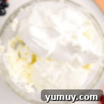 Luscious Chocolate Fruit Delight 5 Beaten cream cheese topped with whipped topping and yogurt in a glass bowl, ready for the next step.