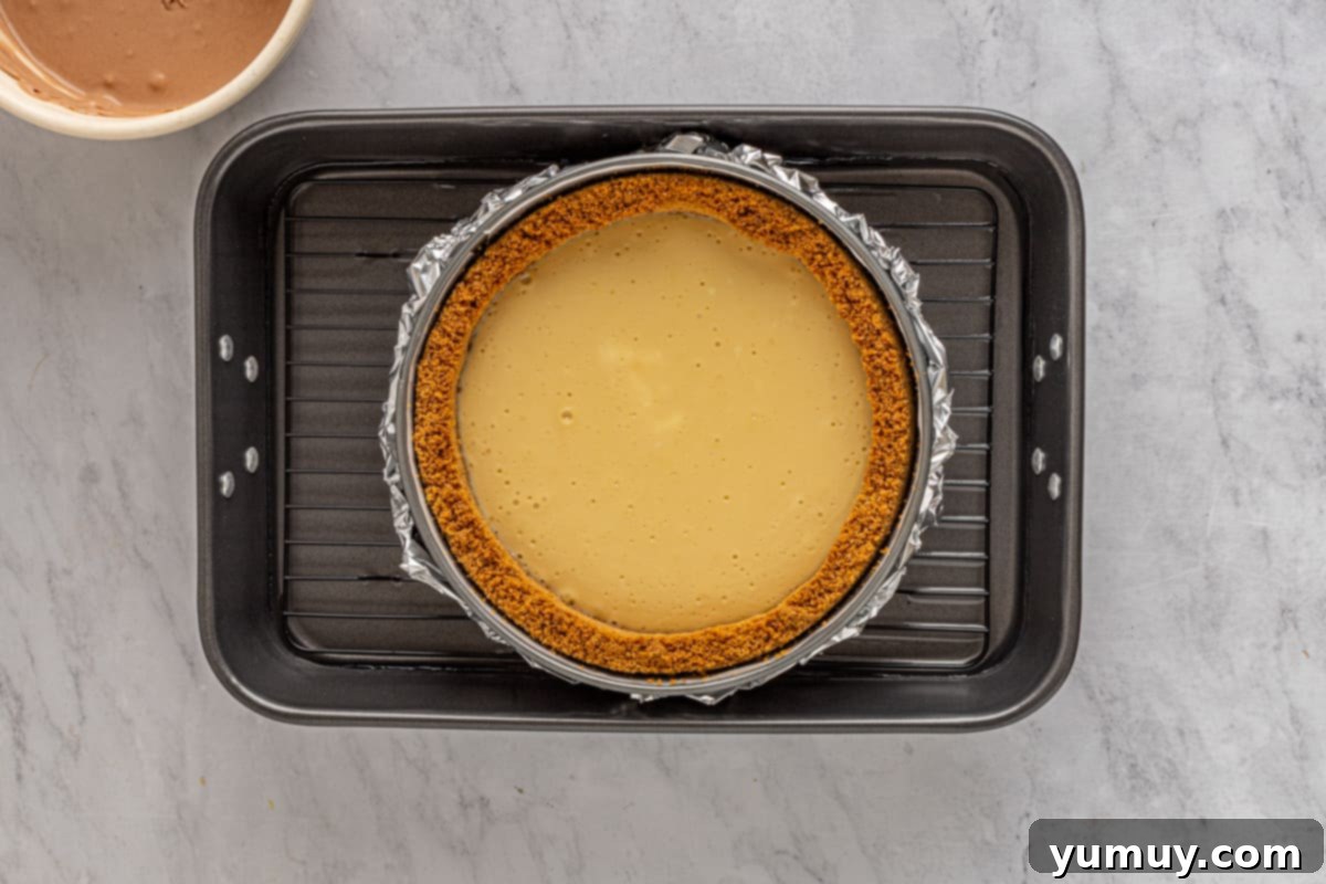 Caramel cheesecake layer in a springform pan, sitting in a water bath in a larger baking pan.