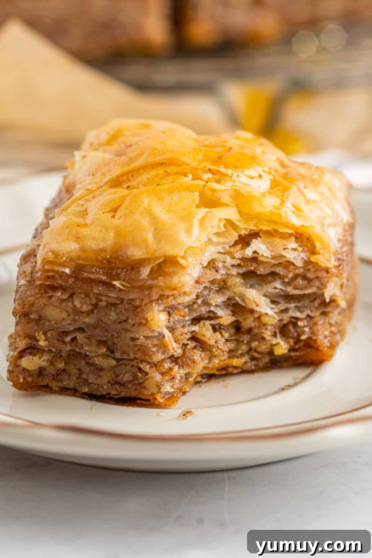 Sweet & Crispy Homemade Greek Baklava 3 A perfectly bitten square of homemade baklava on a white plate, revealing its flaky layers and nutty interior.