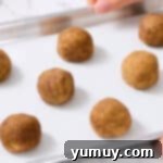 8 cinnamon-sugar coated churro cookie dough balls spread out on a baking sheet.