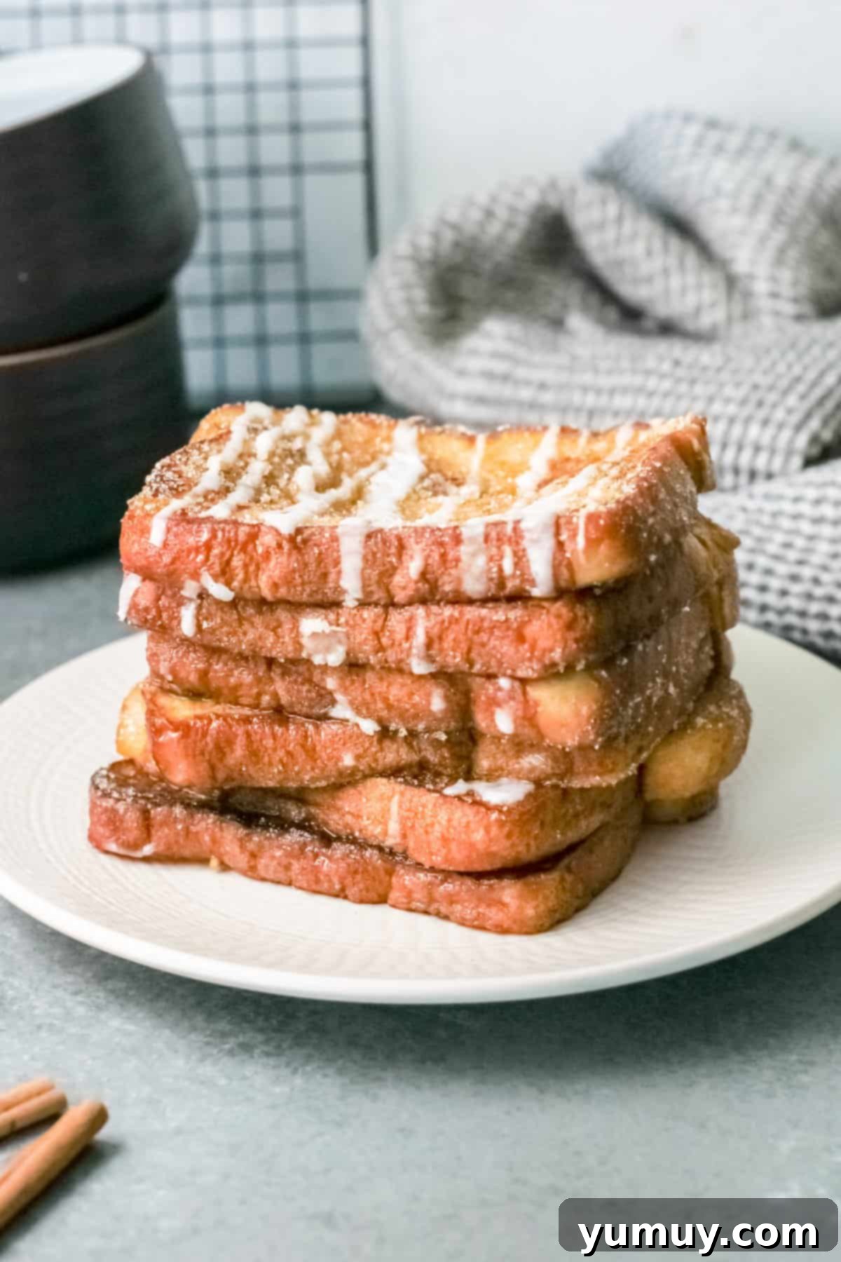 Stacked slices of golden brown churro French toast, dusted with cinnamon sugar, on a plate, ready to be served.