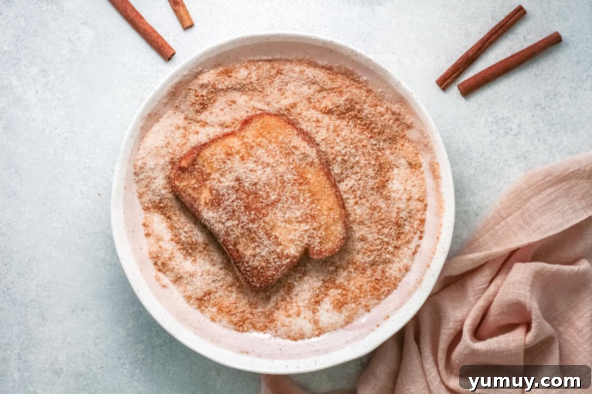 french toast slice being dipped in cinnamon sugar mixture in a white bowl.