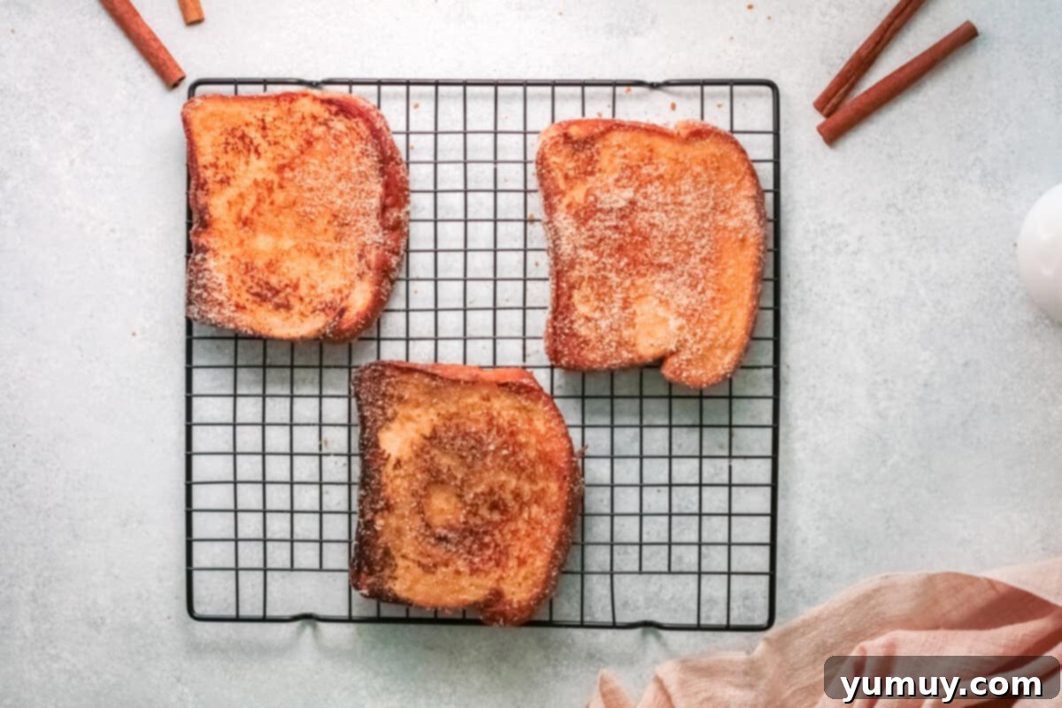 three slices of churro french toast resting on a wire rack after being coated.