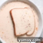 a slice of toast dipped in egg mixture in a white bowl.