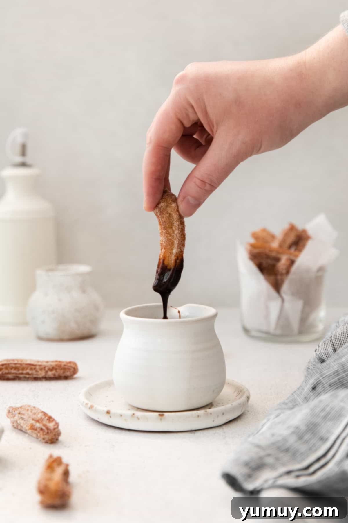 hand dipping a churro into chocolate sauce in a white pot.