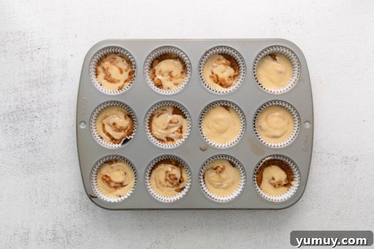 swirled cinnamon swirl cupcake batter in the wells of a lined cupcake tin.