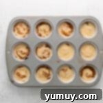 swirled cinnamon swirl cupcake batter in the wells of a lined cupcake tin.