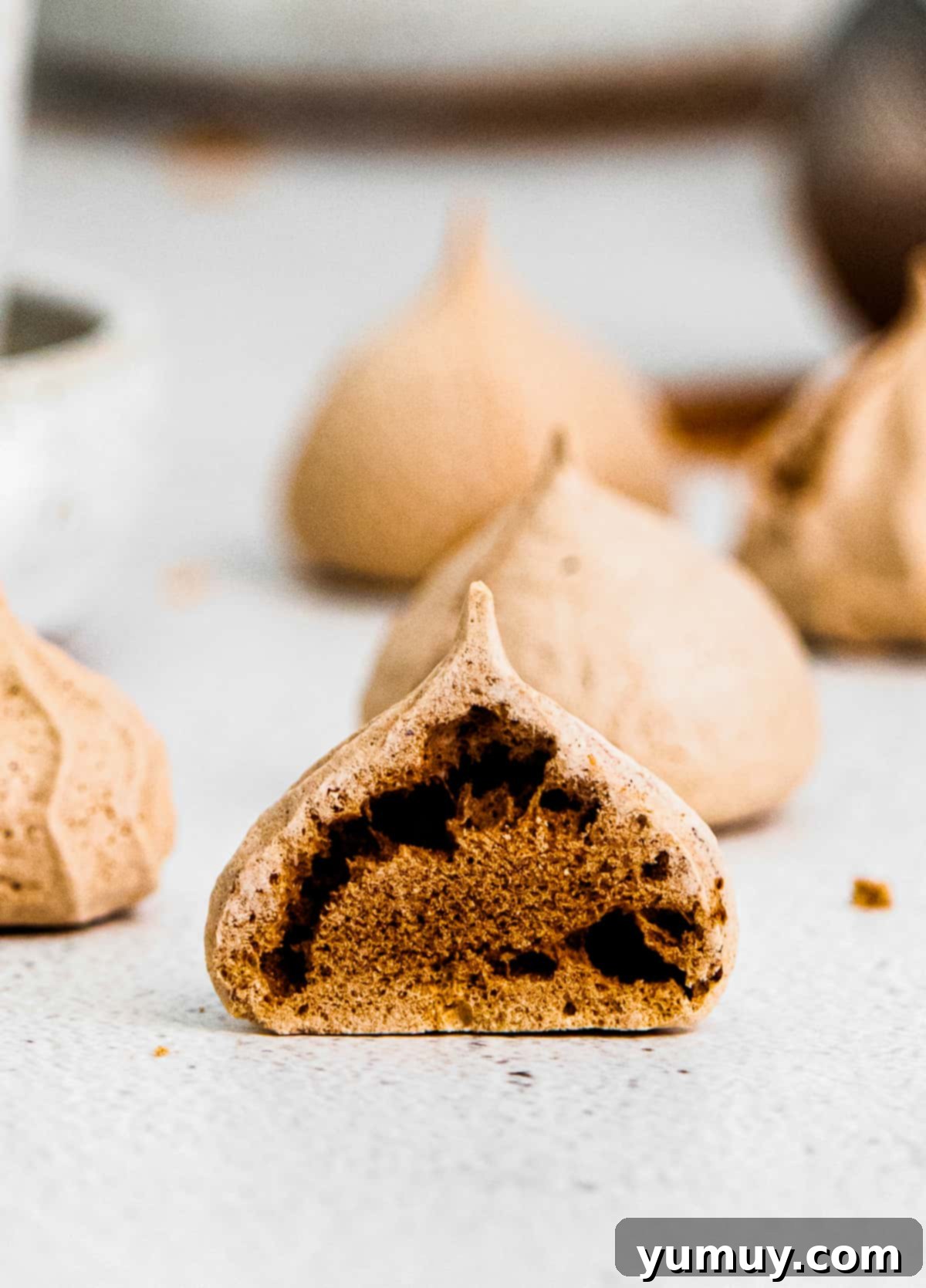 Sliced chocolate meringue cookie revealing its soft, chewy center against a backdrop of whole cookies.