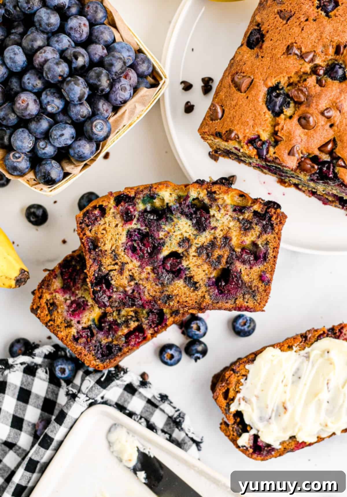 two stacked slices of chocolate chip blueberry banana bread on table next to blueberries
