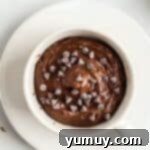 Chocolate cake batter topped with chocolate chips in a white coffee mug.