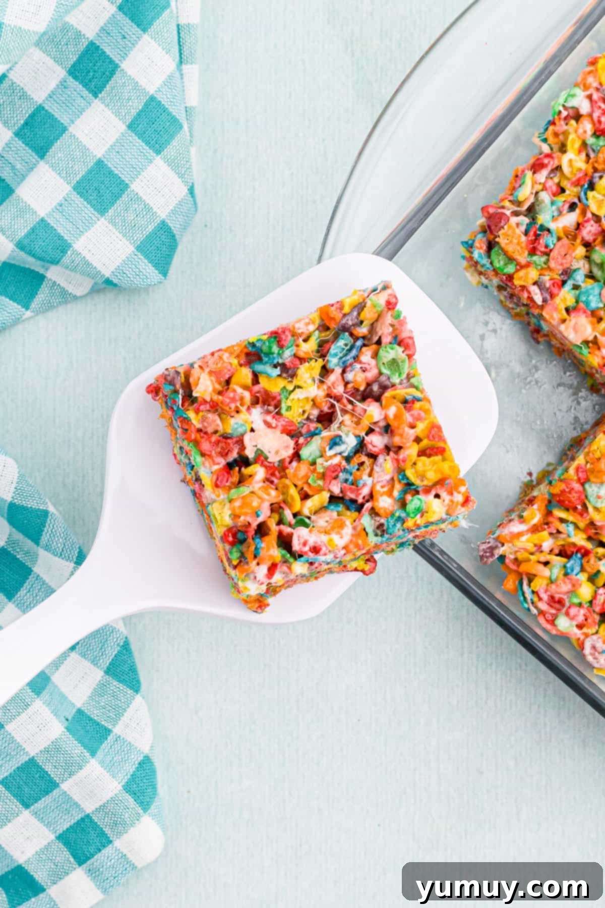Overhead view of a perfectly sliced Fruity Pebbles treat on a white spatula, showcasing its vibrant colors and gooey texture.