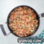 Colorful Fruity Pebbles cereal being stirred into the melted marshmallow and butter in a saucepan.