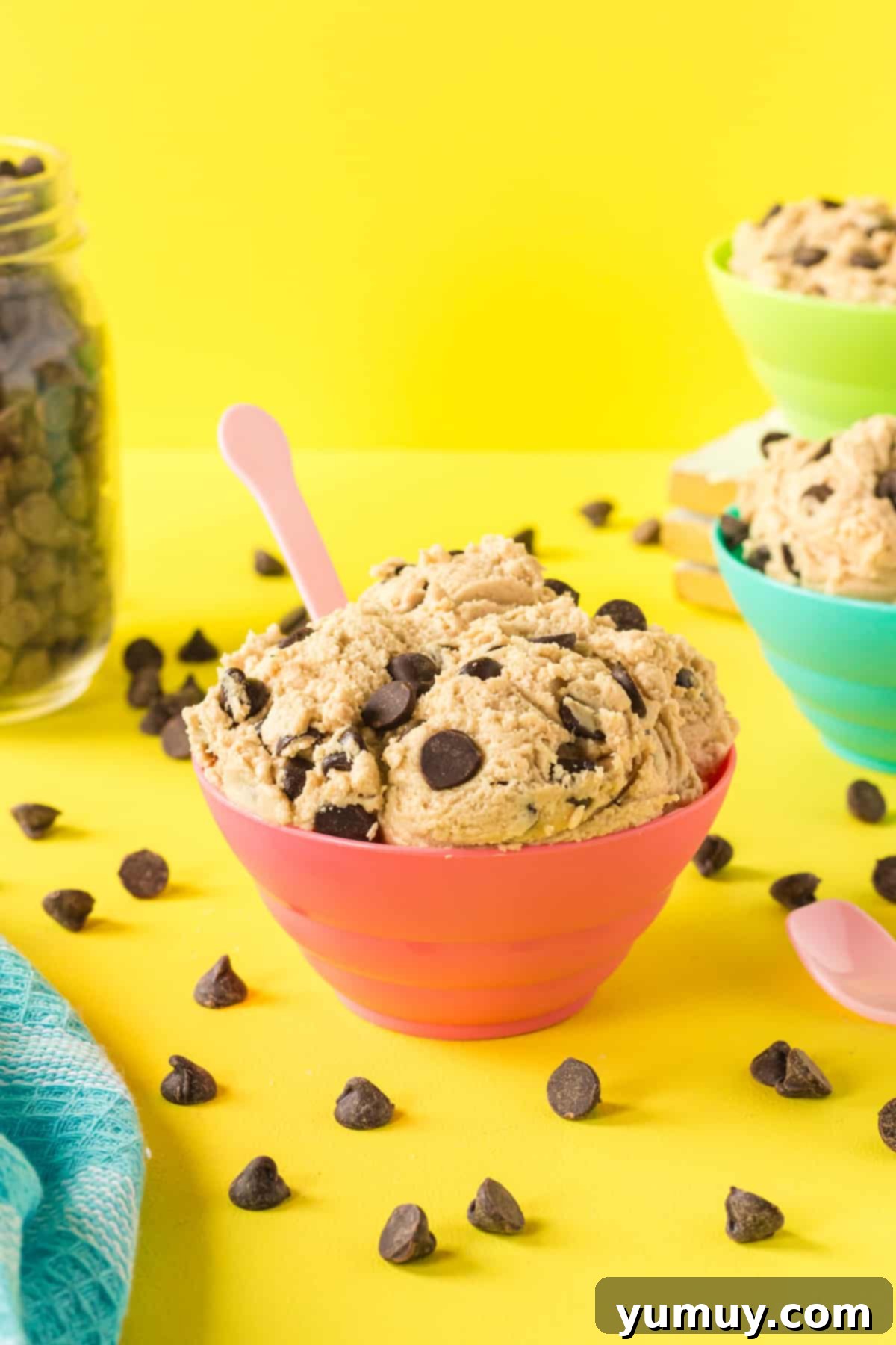 edible chocolate chip cookie dough in a red bowl with a pink spoon.