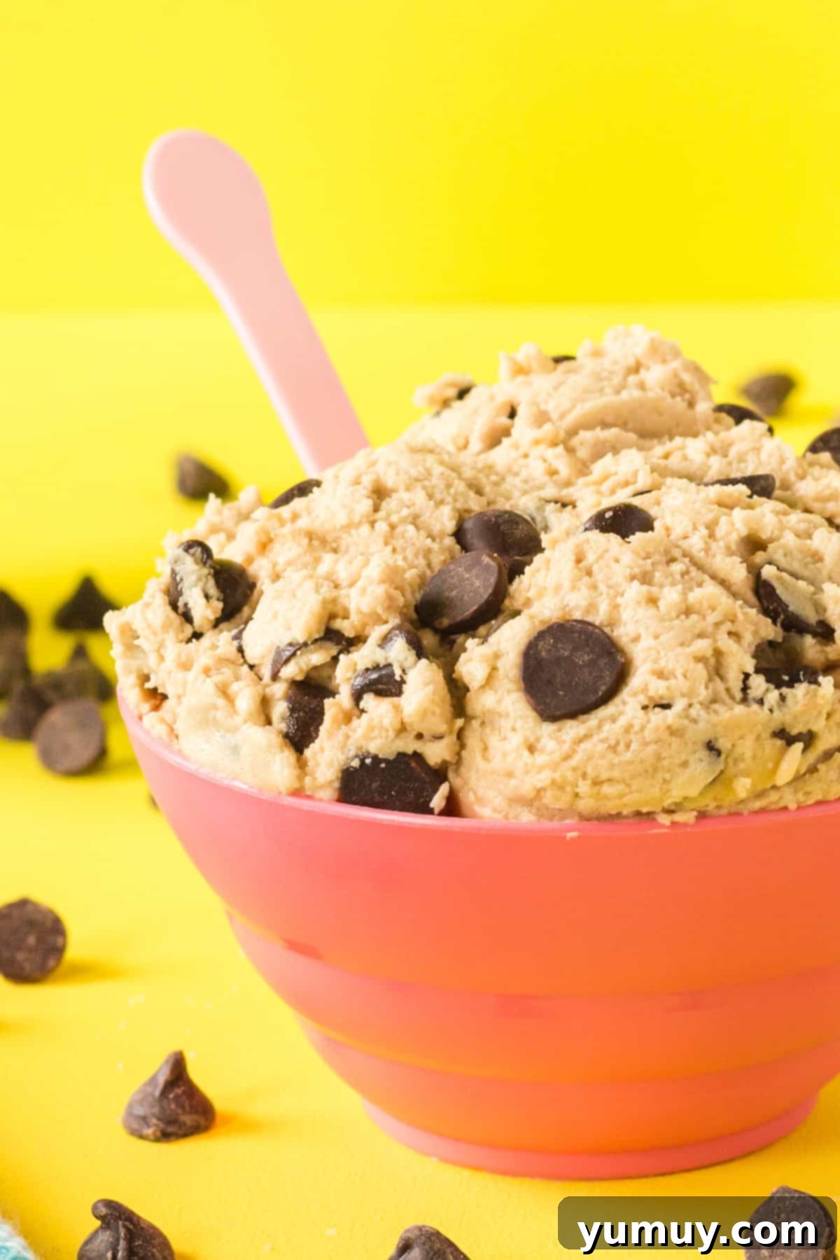 close up of edible chocolate chip cookie dough in a red bowl with a pink spoon.