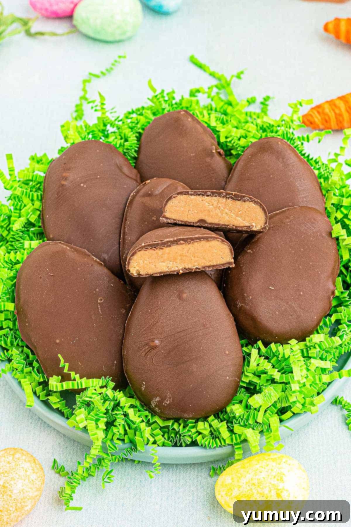 Homemade Reese's style peanut butter eggs on fake grass, one cut in half revealing the creamy peanut butter center.