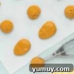 Scoops of peanut butter mixture shaped into perfect little eggs on parchment paper, ready for chilling.