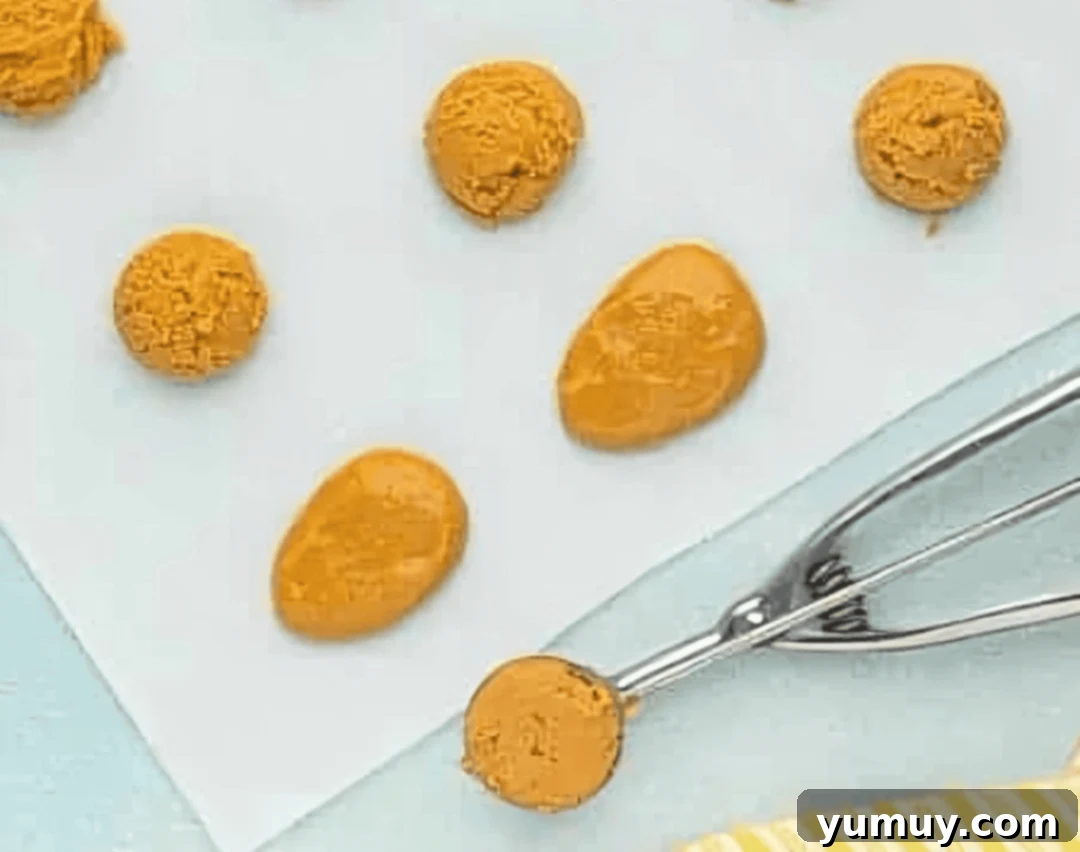 Scoops of creamy peanut butter mixture meticulously shaped into uniform egg forms, arranged on parchment paper.