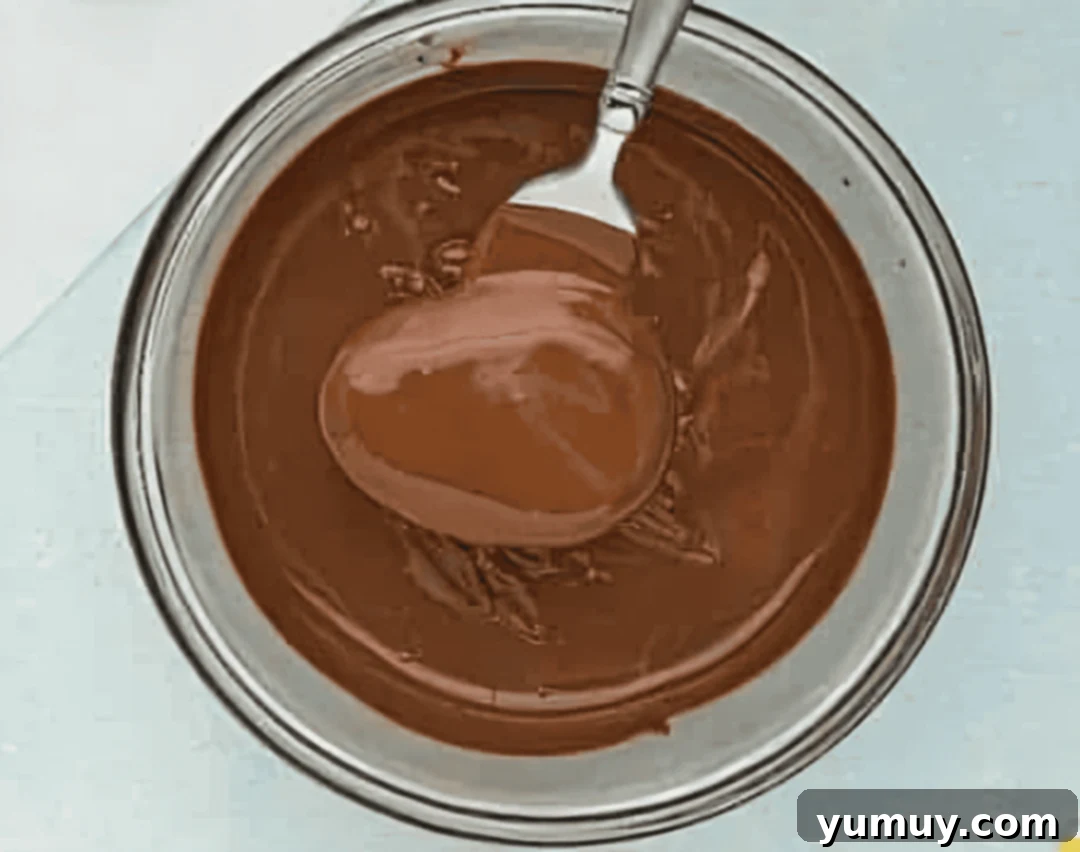 A chocolate-dipped peanut butter egg being lifted from melted chocolate on a fork.