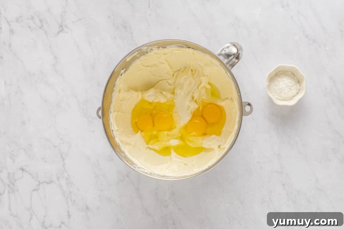 overhead view of eggs added to cheesecake batter in a stainless mixing bowl.