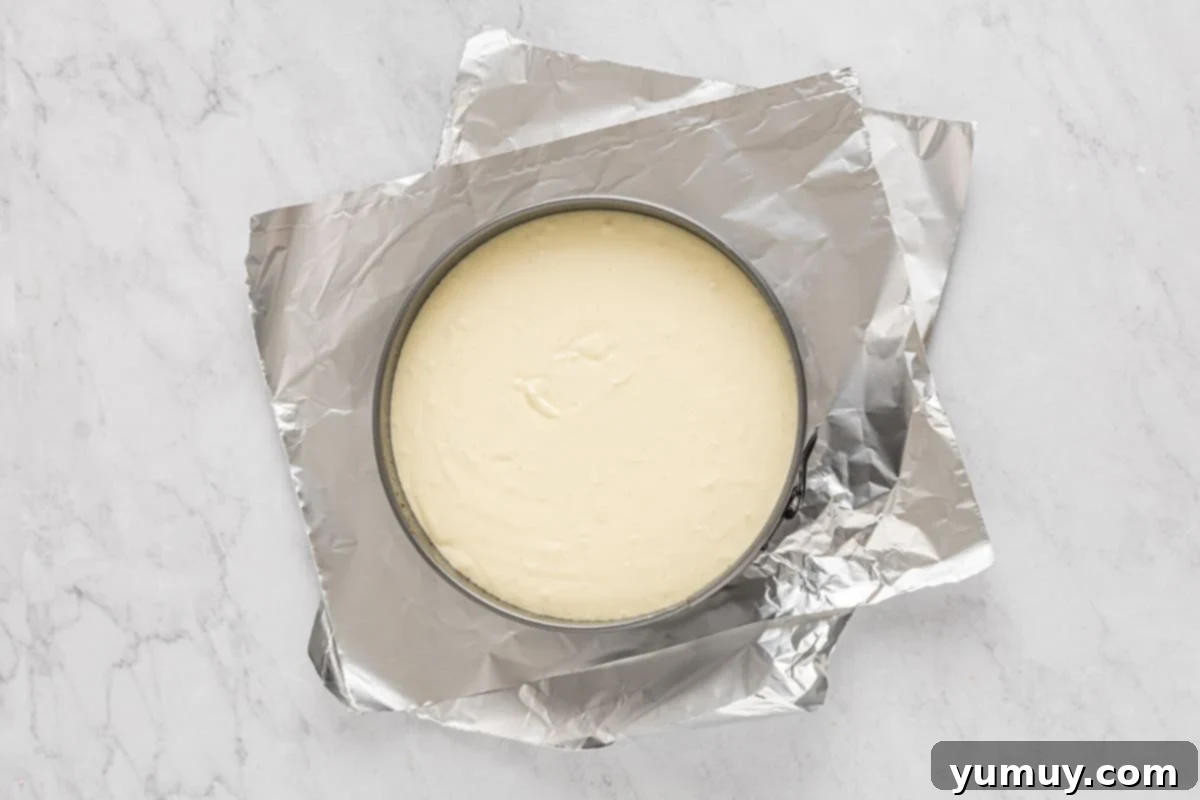 overhead view of creme brulee cheesecake batter in a springform pan on top of sheets of aluminum foil.