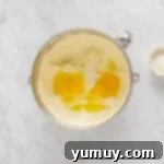 overhead view of eggs added to cheesecake batter in a stainless mixing bowl.