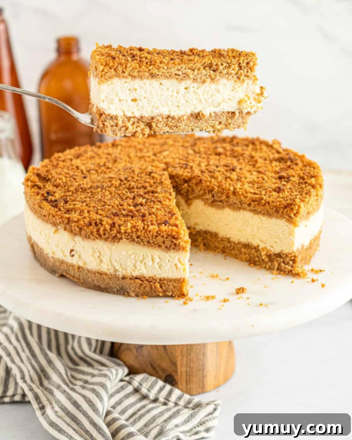 A perfectly sliced double crust cheesecake, revealing creamy filling and two distinct graham cracker crust layers. Held over a whole cheesecake.