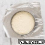 Overhead view of double crust cheesecake batter in a springform pan on top of sheets of aluminum foil.