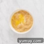 Overhead view of graham cracker crust mixture in a white bowl, ready for pressing.