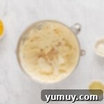 Overhead view of heavy cream, sour cream, salt, and vanilla added to cream cheese in a stainless mixing bowl.