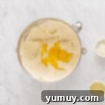 Overhead view of eggs added to double crust cheesecake batter in a stainless mixing bowl.
