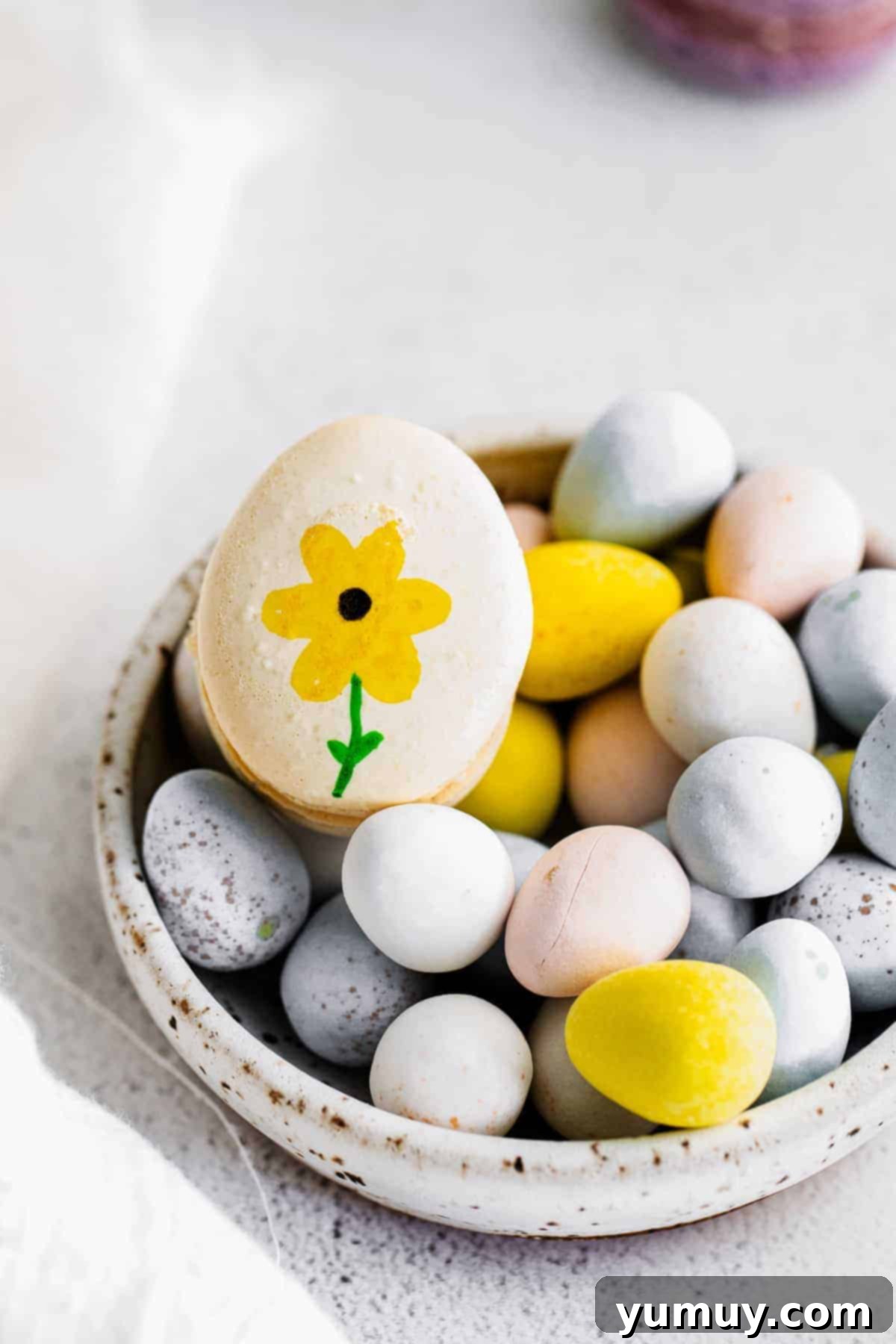 Springtime Macaron Delights 3 An intricately decorated Easter egg macaron resting among chocolate eggs, highlighting its festive charm.