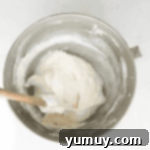Springtime Macaron Delights 5 Macaron batter in a stainless steel mixing bowl, being gently folded with a rubber spatula, demonstrating the macaronage technique.