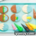 Whimsical Easter Egg Cookies 11 Overhead view of six frosted Easter egg sugar cookies on a blue baking sheet with piping bags filled with colored frosting, showing initial decorations.