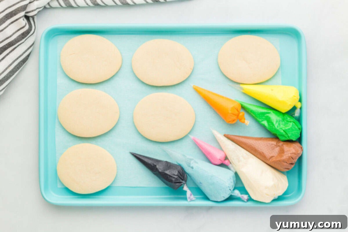 Whimsical Easter Egg Cookies 17 Overhead view of six Easter egg sugar cookies on a blue baking sheet, accompanied by piping bags filled with various colored frostings.