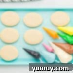 Whimsical Easter Egg Cookies 10 Overhead view of six Easter egg sugar cookies on a blue baking sheet with piping bags filled with colored frosting.