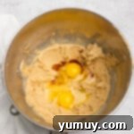 overhead view of eggs and vanilla added to easter basket cookie cup dough in a stainless mixing bowl.