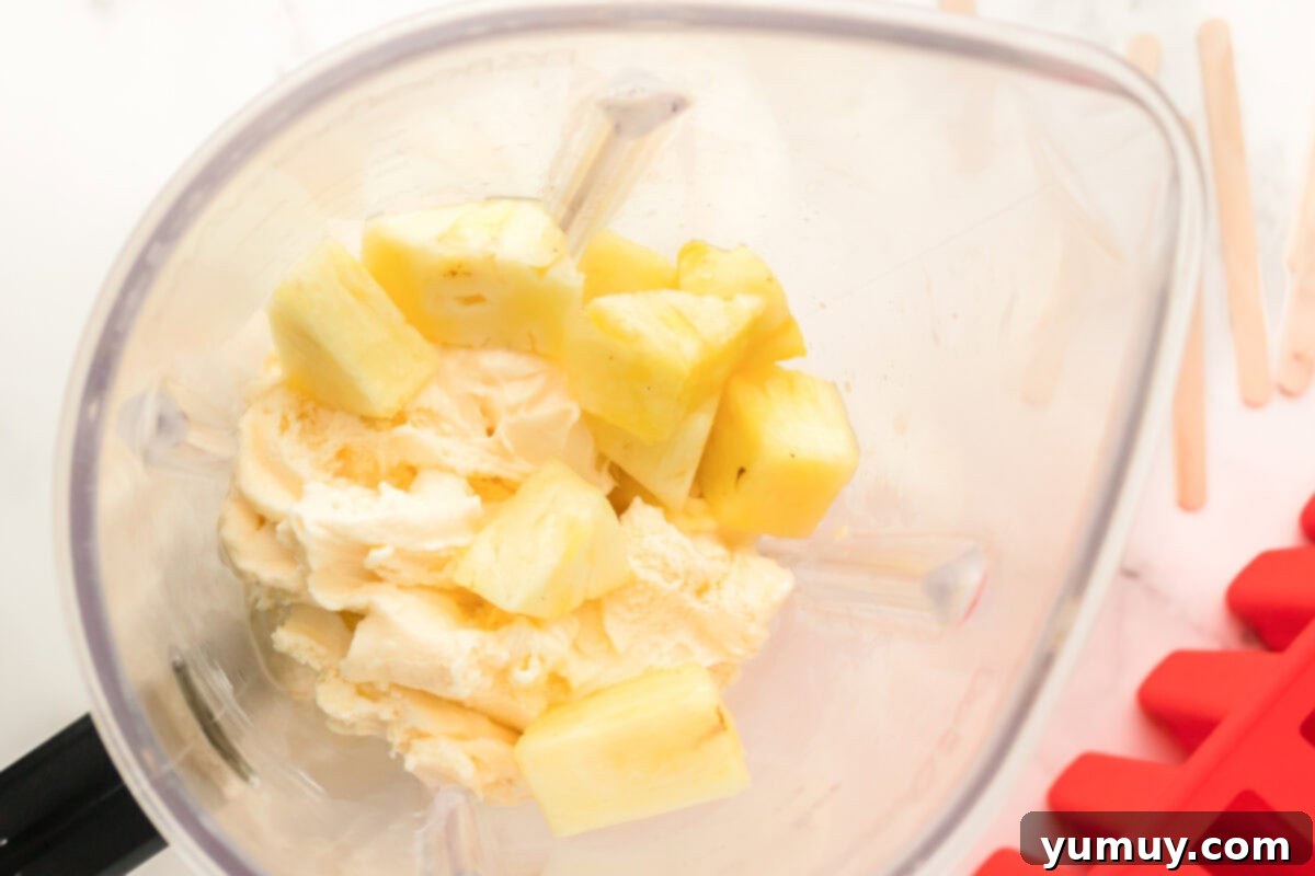 Pineapple chunks and vanilla ice cream blending into a smooth mixture for popsicles.