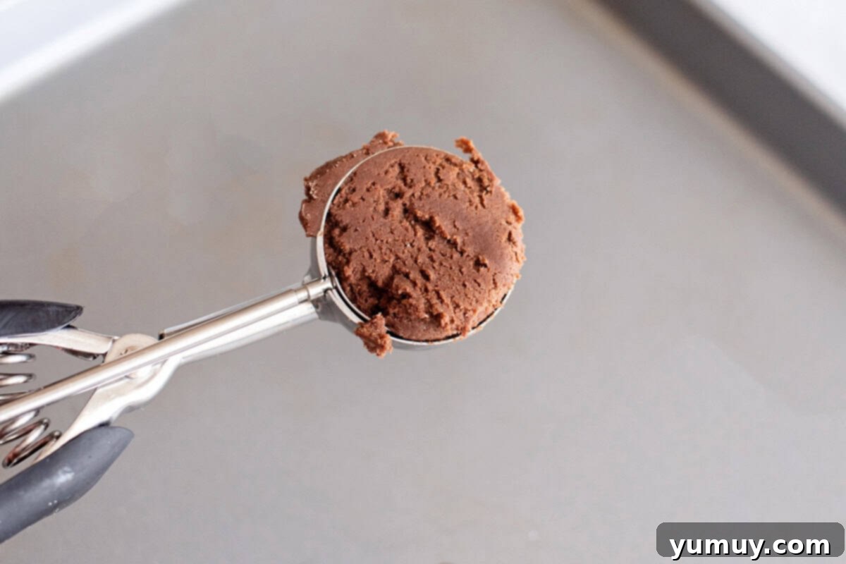 Gooey Chocolate Marshmallow Cookies 18 Scooping portions of chocolate cookie dough using a cookie scoop, highlighting the consistent size of each portion.