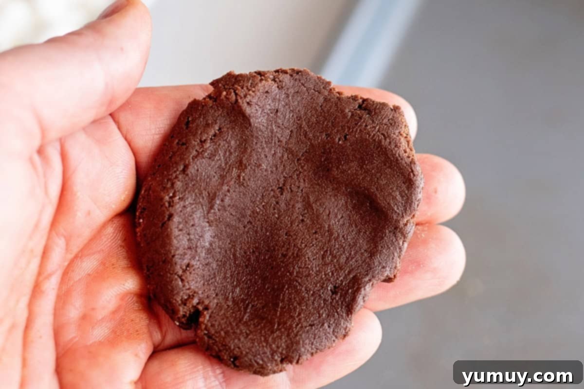 Gooey Chocolate Marshmallow Cookies 19 Hand holding up a flattened piece of chocolate cookie dough, ready for stuffing.