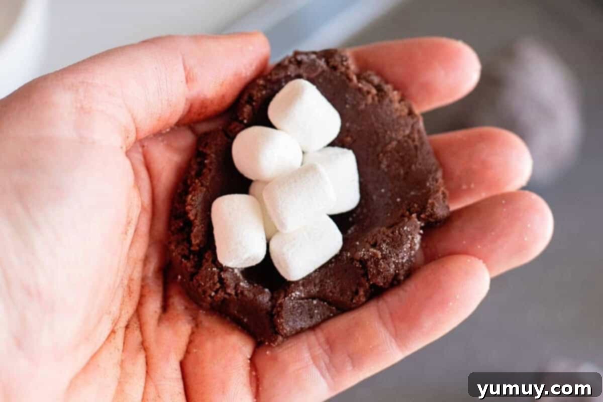 Gooey Chocolate Marshmallow Cookies 20 Hand holding a portion of cookie dough filled with mini marshmallows, ensuring they are well-covered.