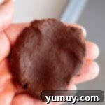 Gooey Chocolate Marshmallow Cookies 9 Hand holding up a flattened piece of chocolate cookie dough, ready for stuffing.