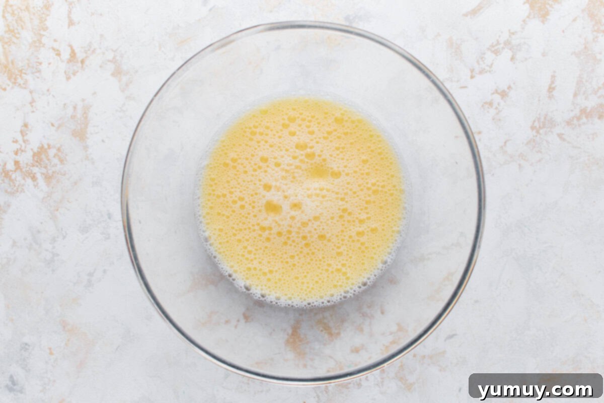 The liquid mixture of water, oil, and eggs in a glass bowl, perfectly whisked.