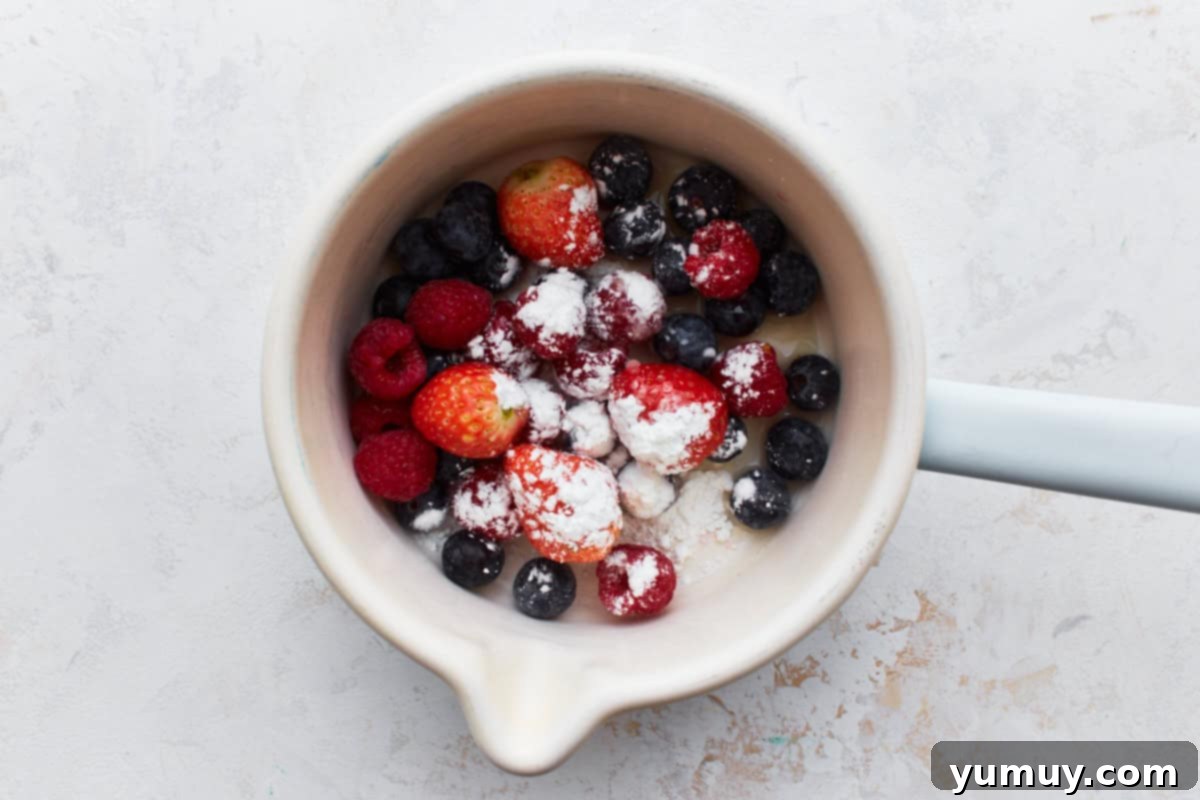 A saucepan filled with fresh mixed berries, lemon juice, and cornstarch, ready to be cooked.