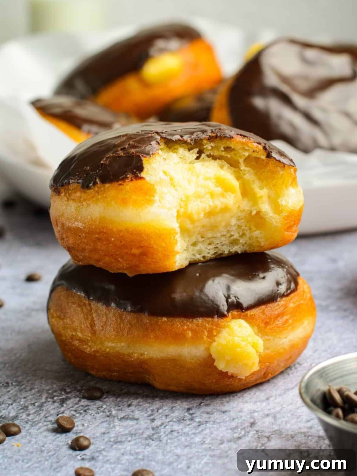 Boston Cream Delights 2 Stacked Boston Cream Donuts, showcasing their fluffy texture, rich vanilla pastry cream filling, and decadent chocolate glaze.