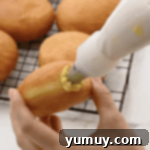 Boston Cream Delights 15 A Boston Cream Donut being filled with vanilla pastry cream using a piping bag.