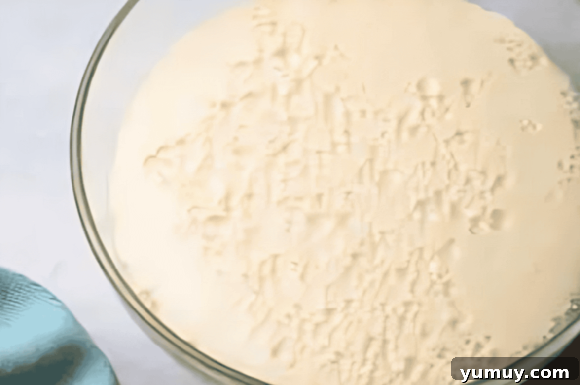 Boston Cream Delights 18 Foamy yeast mixture proofing in a clear glass bowl, indicating active yeast.