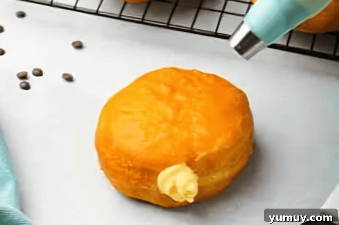 Boston Cream Delights 25 A donut being carefully filled with creamy vanilla pastry cream using a piping bag.