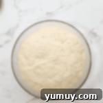 Boston Cream Delights 8 Fully proofed donut dough, visibly expanded in a glass bowl, covered with plastic wrap.